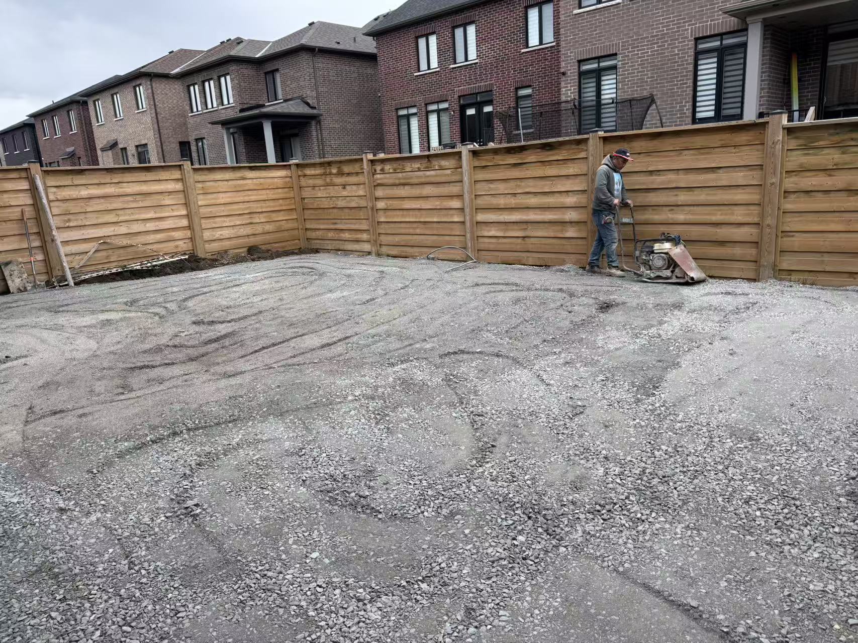 Crew member compacting the stone base with a plate compactor