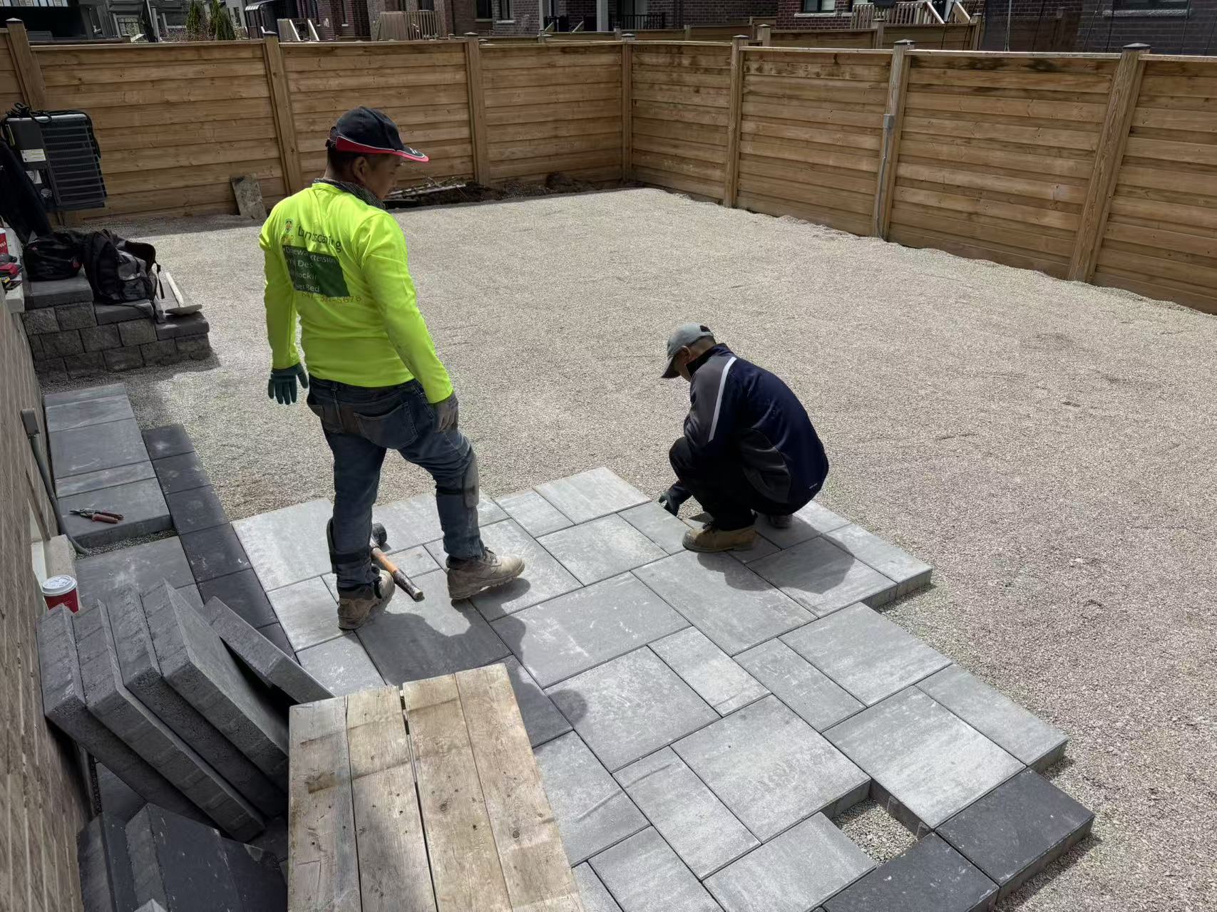 Two crew members hand-laying interlocking pavers in a Roman pattern