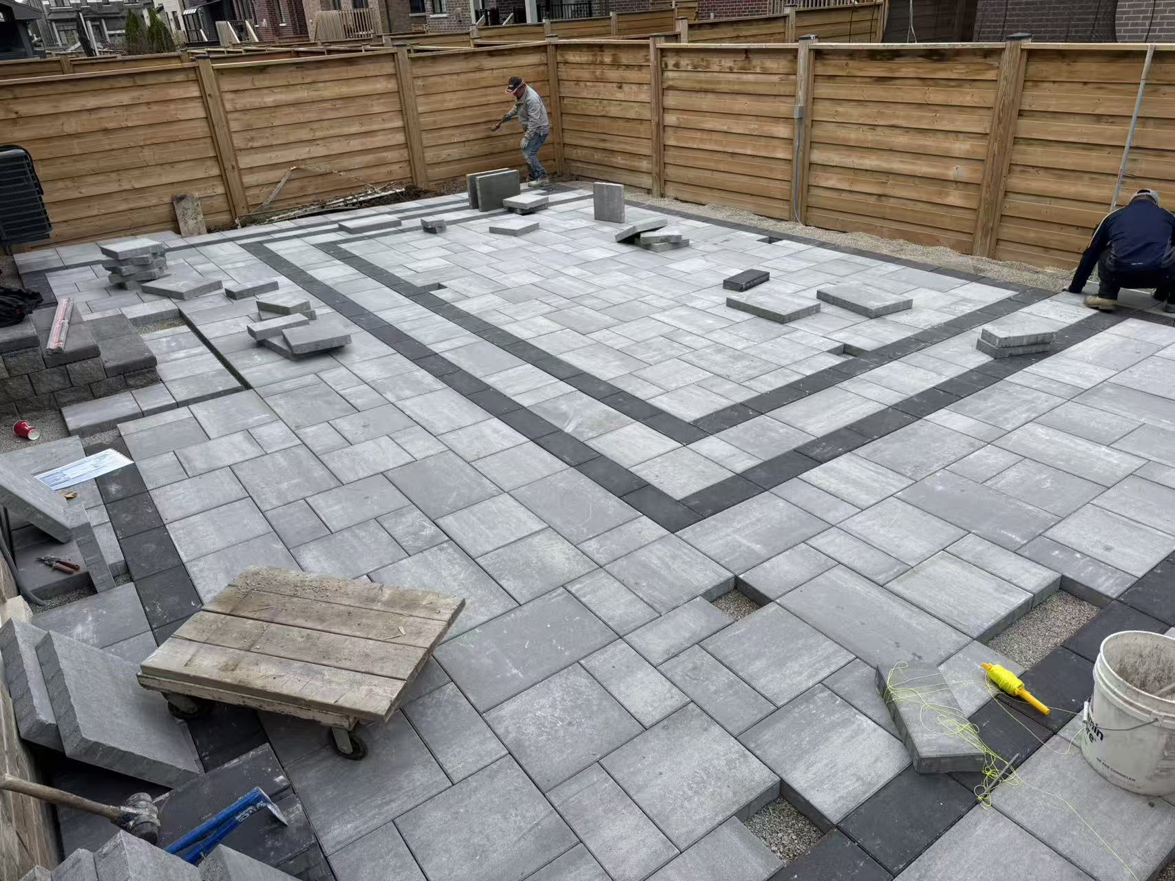 Overhead view of the paver field mid-install, with the dark banded border running through a Roman pattern