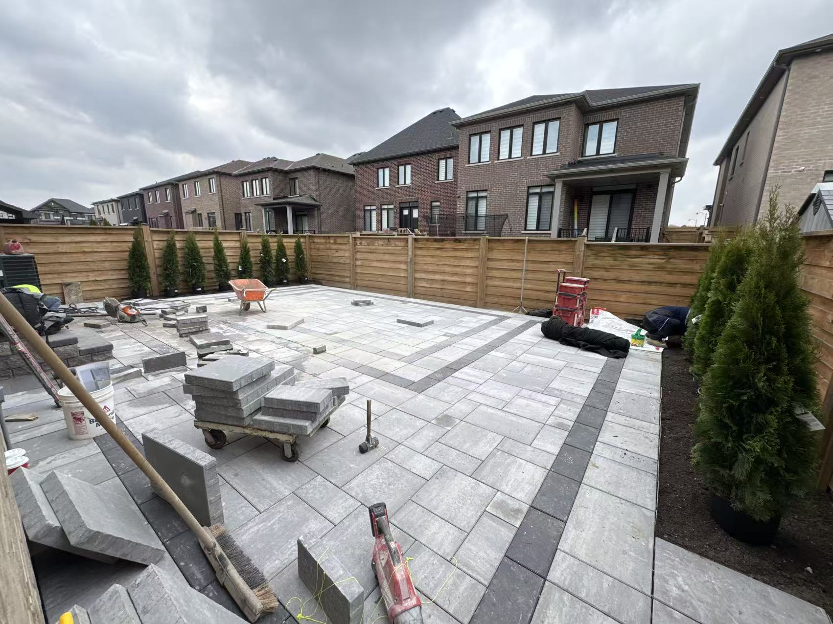 Finished paver patio with a banded border, freshly planted cedars along the back fence